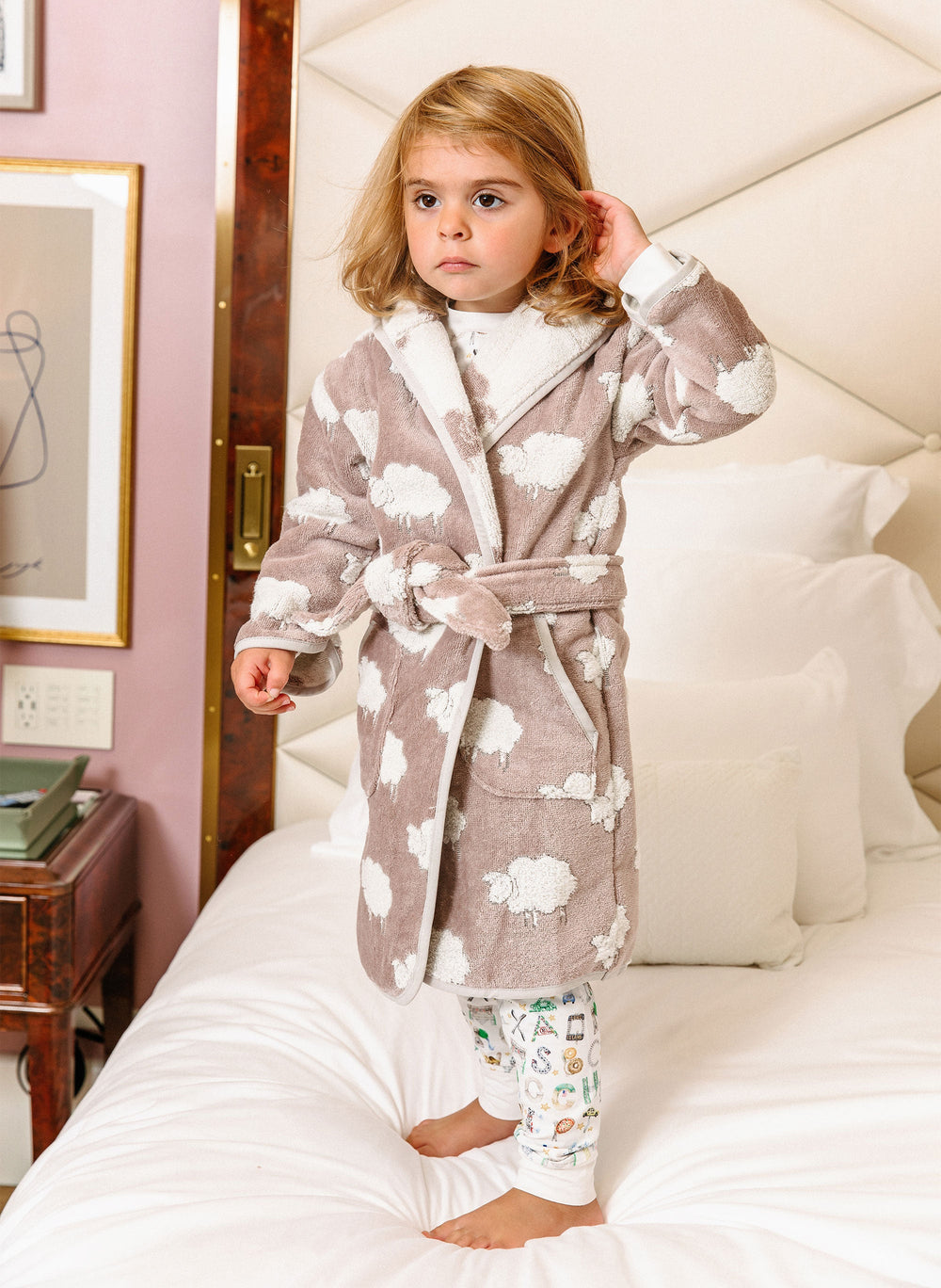Front view of Sweet Sheep bathrobe on child, organic cotton terry with white sheep pattern, hood and tied belt on bed