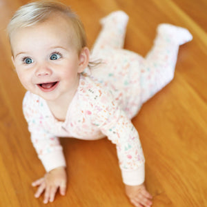 Top view of pink Après Ski Zip Baby Onesie showcasing hand-drawn winter print and pink trim on a baby on wood floor
