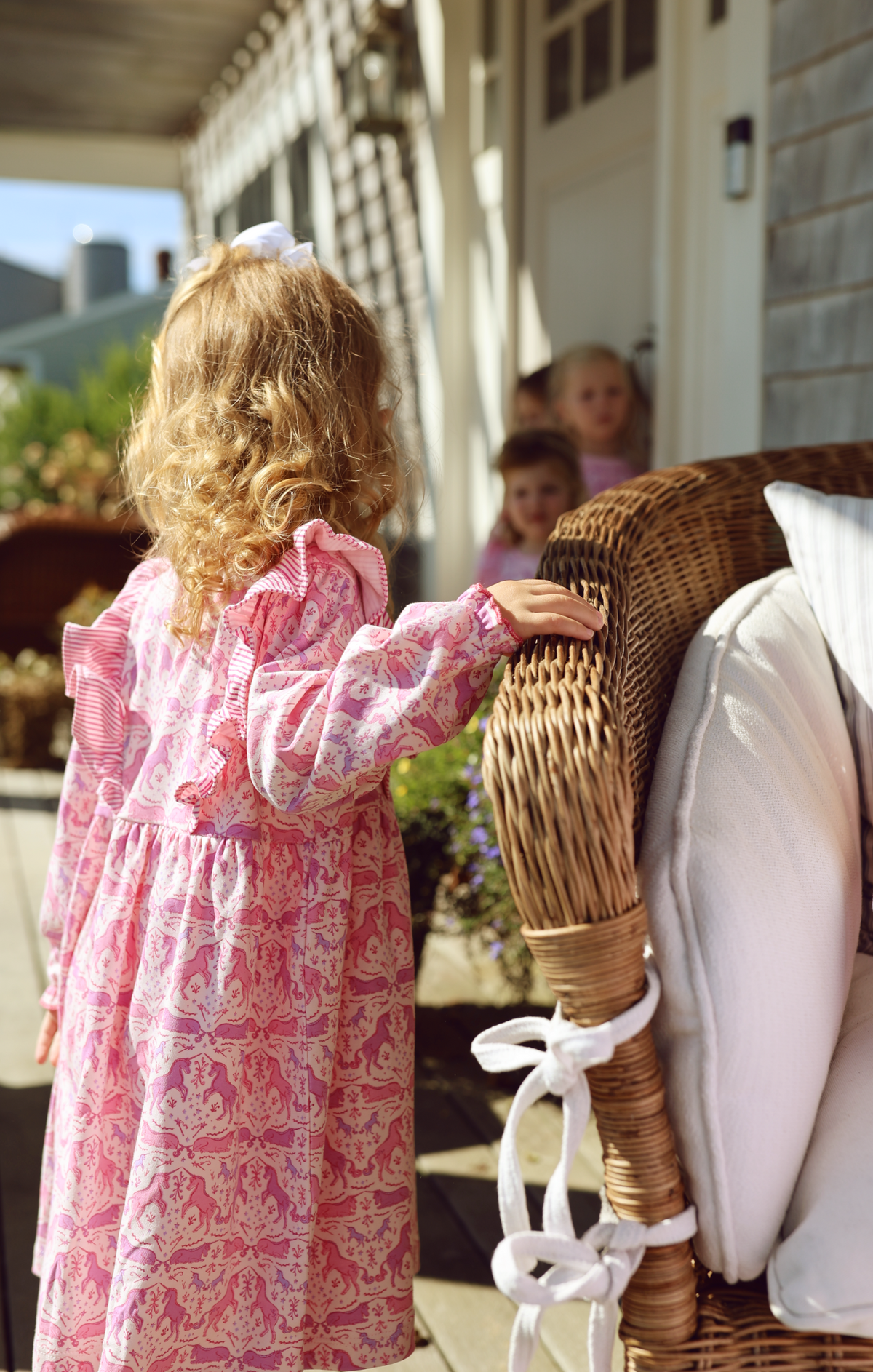 Back view of Unicorns Lily Long Sleeve Play Dress showcasing pink unicorn print and ruffle details beside a wicker stroller