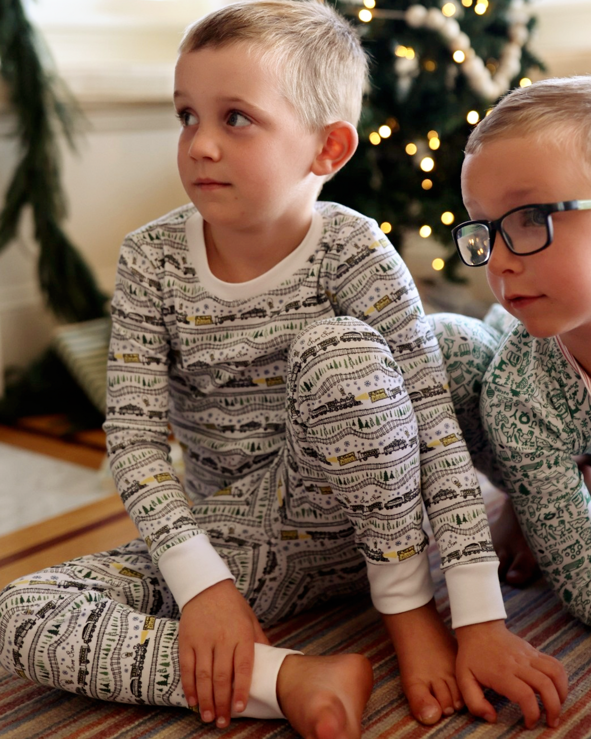 Front view of Christmas Trains Kids Pajamas set showcasing hand-drawn train print and snug fit on children beside a Christmas tree
