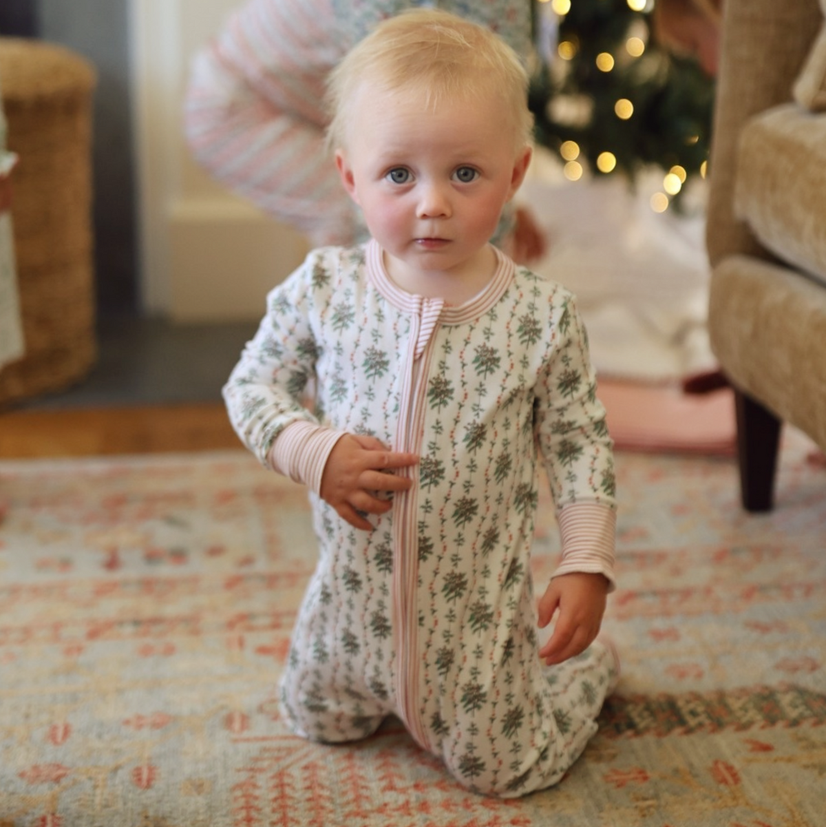 Front view of the cream Holly Baby Snap Onesie showcasing hand-drawn greenery and red berry print on a baby indoors