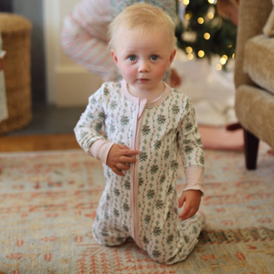 Front view of the cream Holly Baby Snap Onesie showcasing hand-drawn greenery and red berry print on a baby indoors