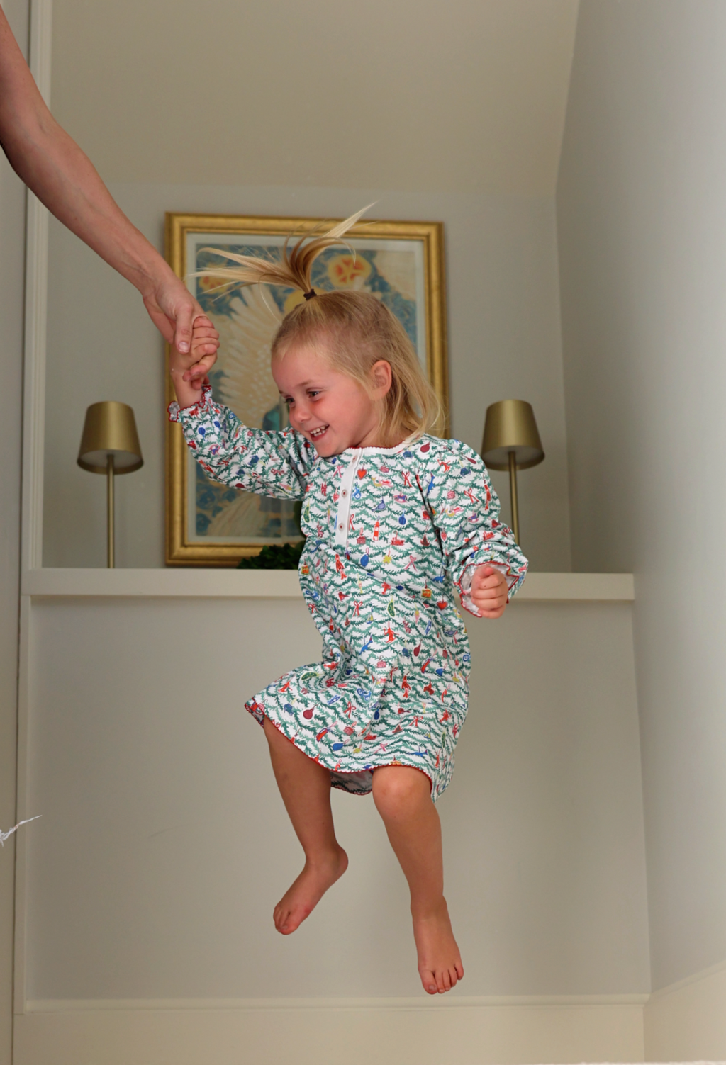 Front view of Oh Christmas Tree Girls Tess Lounge Dress showcasing a hand-drawn evergreen and ornament print on a jumping child indoors