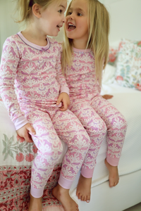 Front view of pink two-piece unicorn kids pajamas showing long sleeves and cuffed pants on two children indoors