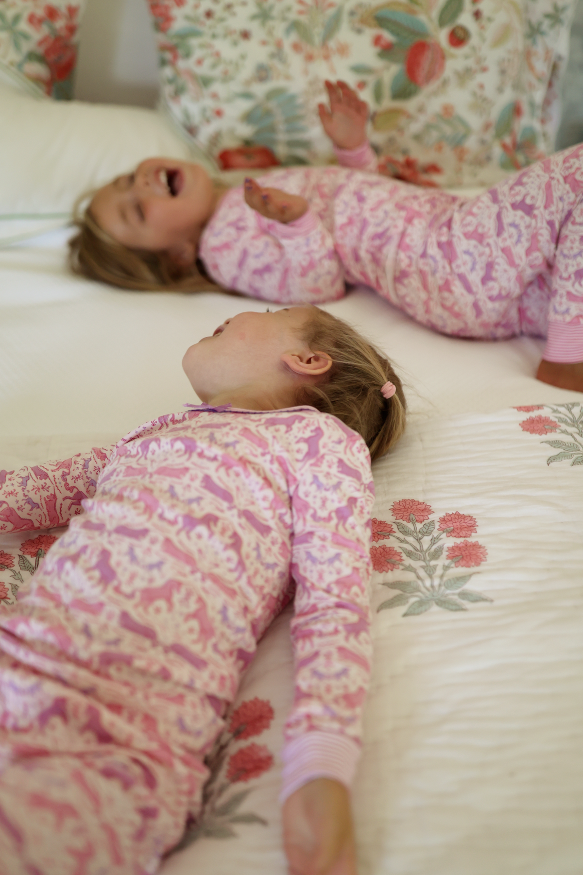 Top view of two children wearing matching pink unicorn two-piece kids pajamas, showcasing the patterned print on a floral bed