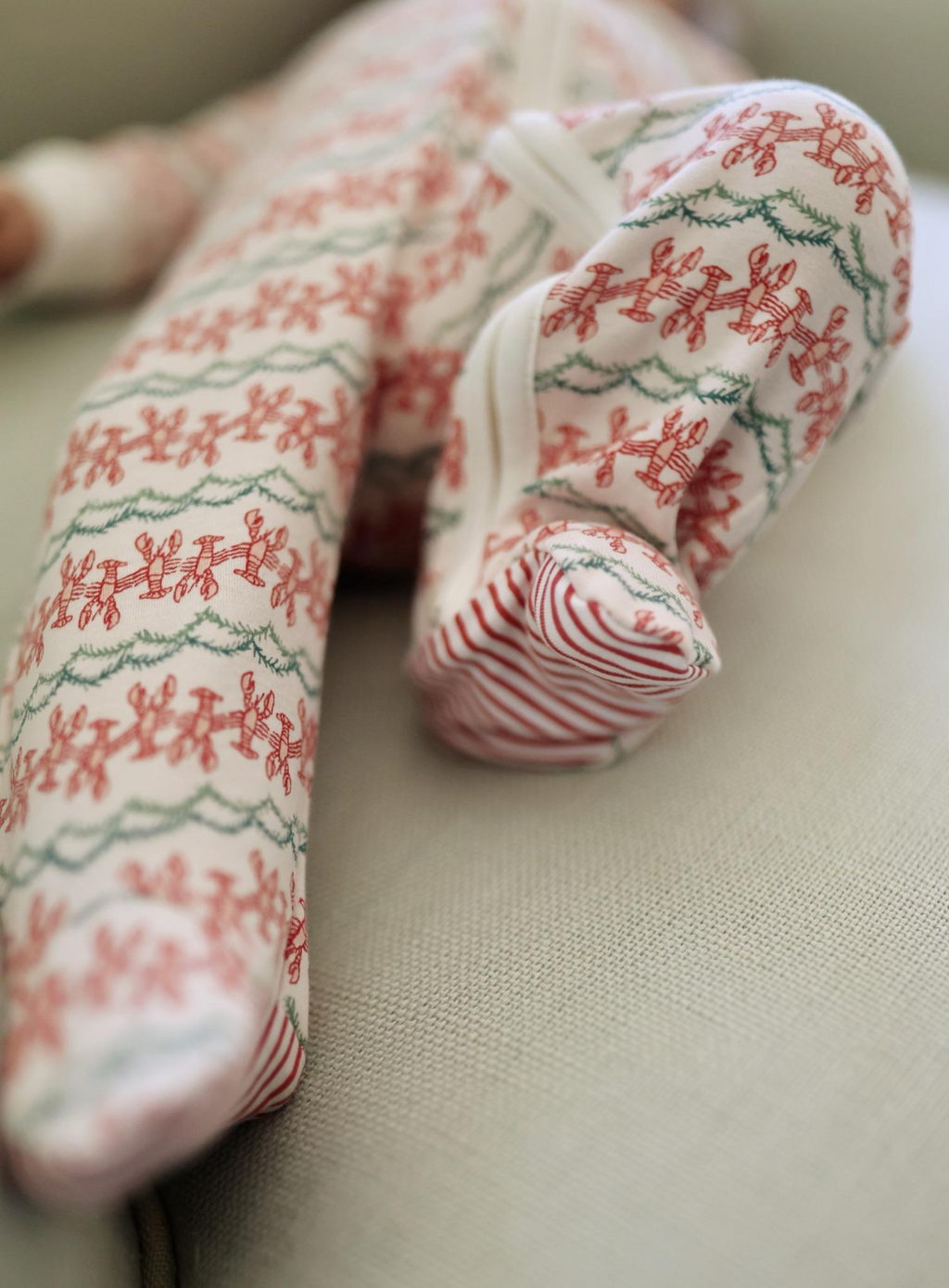 Close-up of Christmas Lobsters Zip Baby Onesie showcasing lobster print and red-and-white striped foot on a neutral background