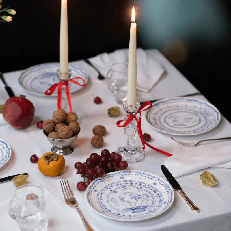 Element Le Feu porcelain plate on a white linen table with grapes, walnuts, a persimmon, and lit taper candles