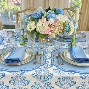 Elegant table setting with floral centerpiece, blue and white patterned tablecloth, and silverware.