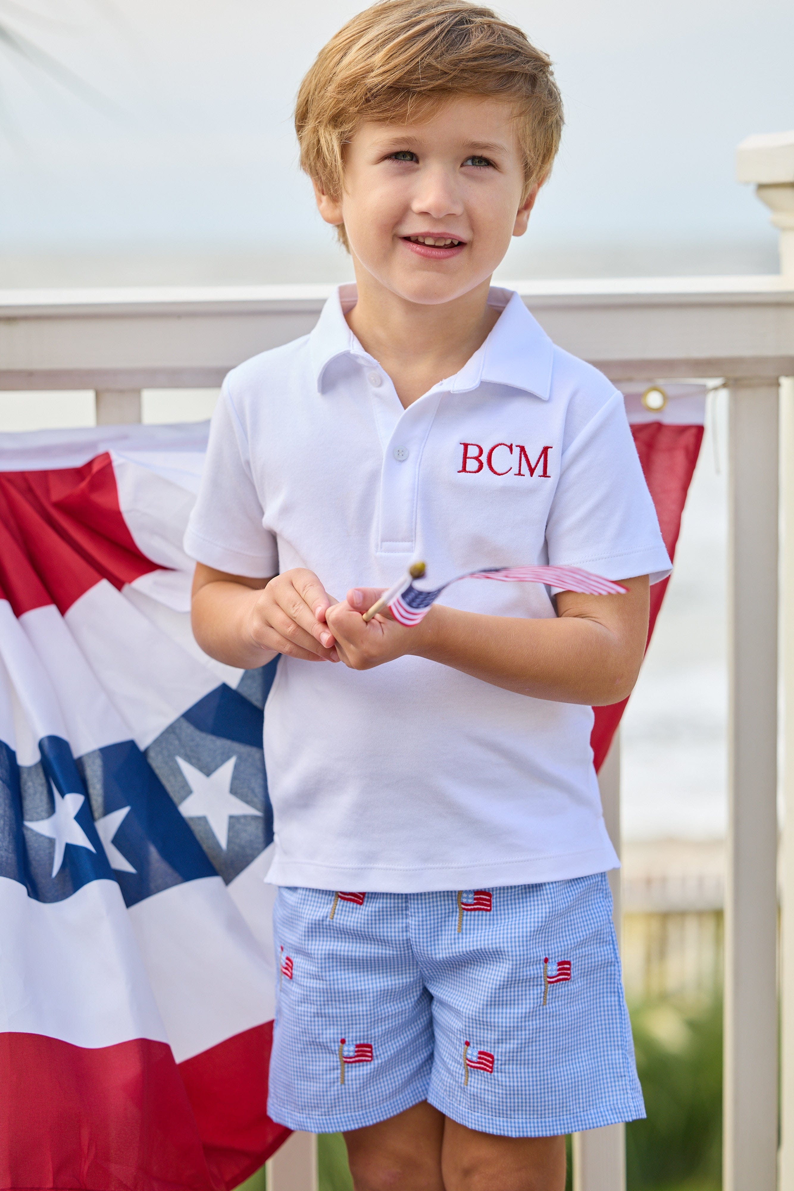 Little English traditional children's clothing.  Blue gingham shorts with all-over American flag embroidery for boys.  Boy's shorts for 4th of July.