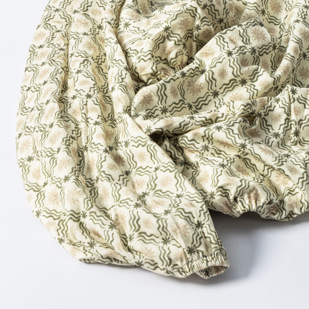 Close-up of a GOTS certified organic brushed cotton crib sheet in Juniper Star, showing its cream and green pattern on white