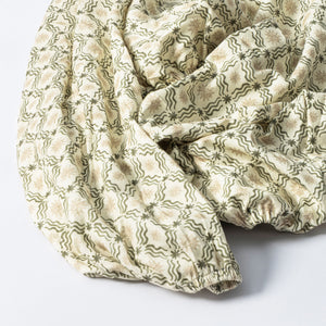 Close-up of a GOTS certified organic brushed cotton crib sheet in Juniper Star, showing its cream and green pattern on white