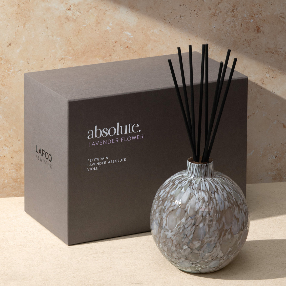 Front view of Lavender Flower Absolute Diffuser showcasing hand blown Macchia glass and black reeds with product box behind