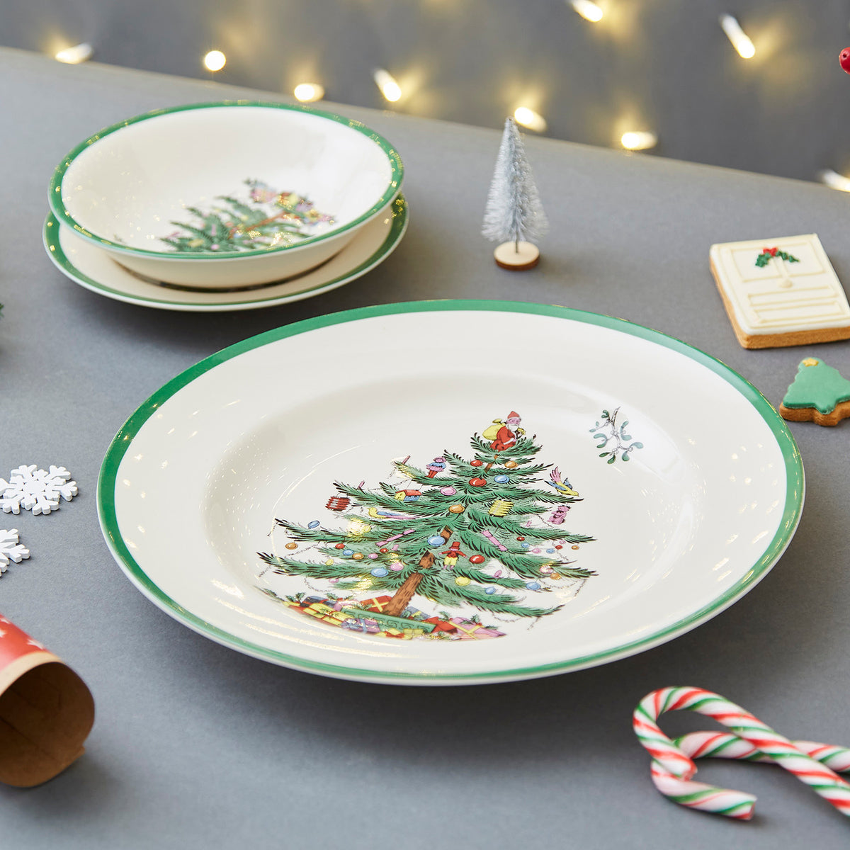 Close-up of 10.5-inch Christmas Tree dinner plate showing tree motif and green rim on gray tabletop with cookies