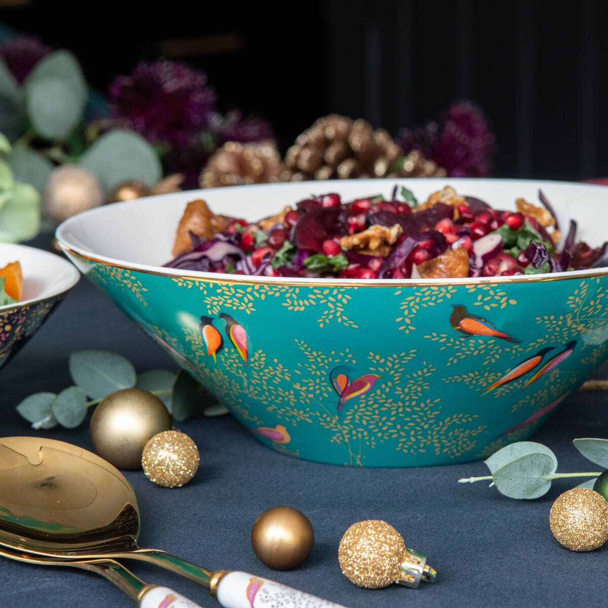 Close-up of Sara Miller Chelsea salad bowl showcasing teal bird pattern and 22K gold detailing with salad and festive decor
