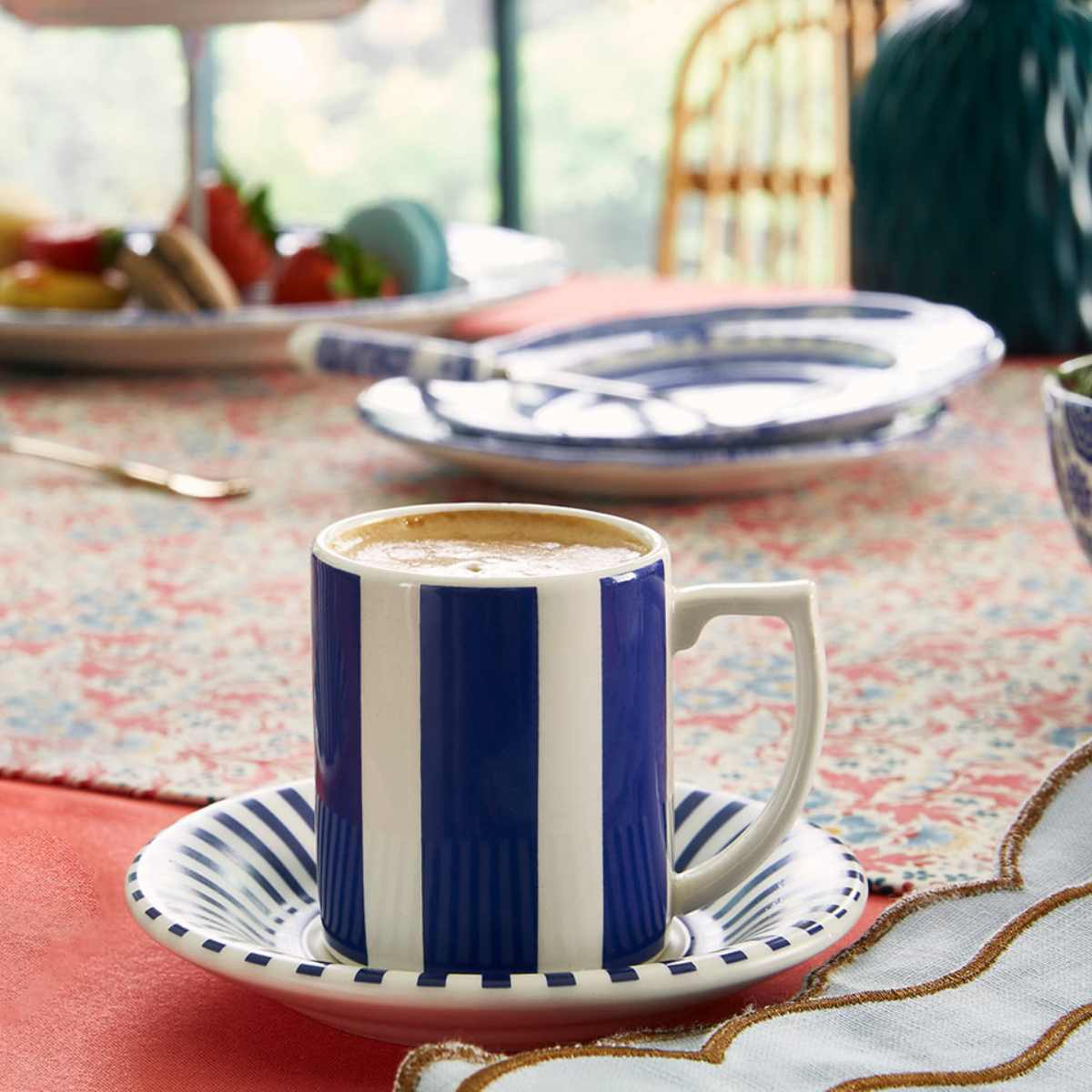 Front view of Steccato Bold Espresso Cup and Saucers, Set of 4 showcasing cobalt blue stripes with a dining table background