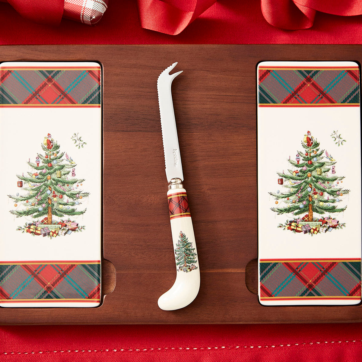 Top view of 13 in Christmas Tree Tartan cheese board with two tree-print ceramic plates and tartan-handled knife on walnut