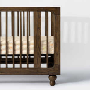 Close-up of Nate Berkus Autumn Stripe crib sheet in GOTS certified organic brushed cotton, shown in a dark wood crib