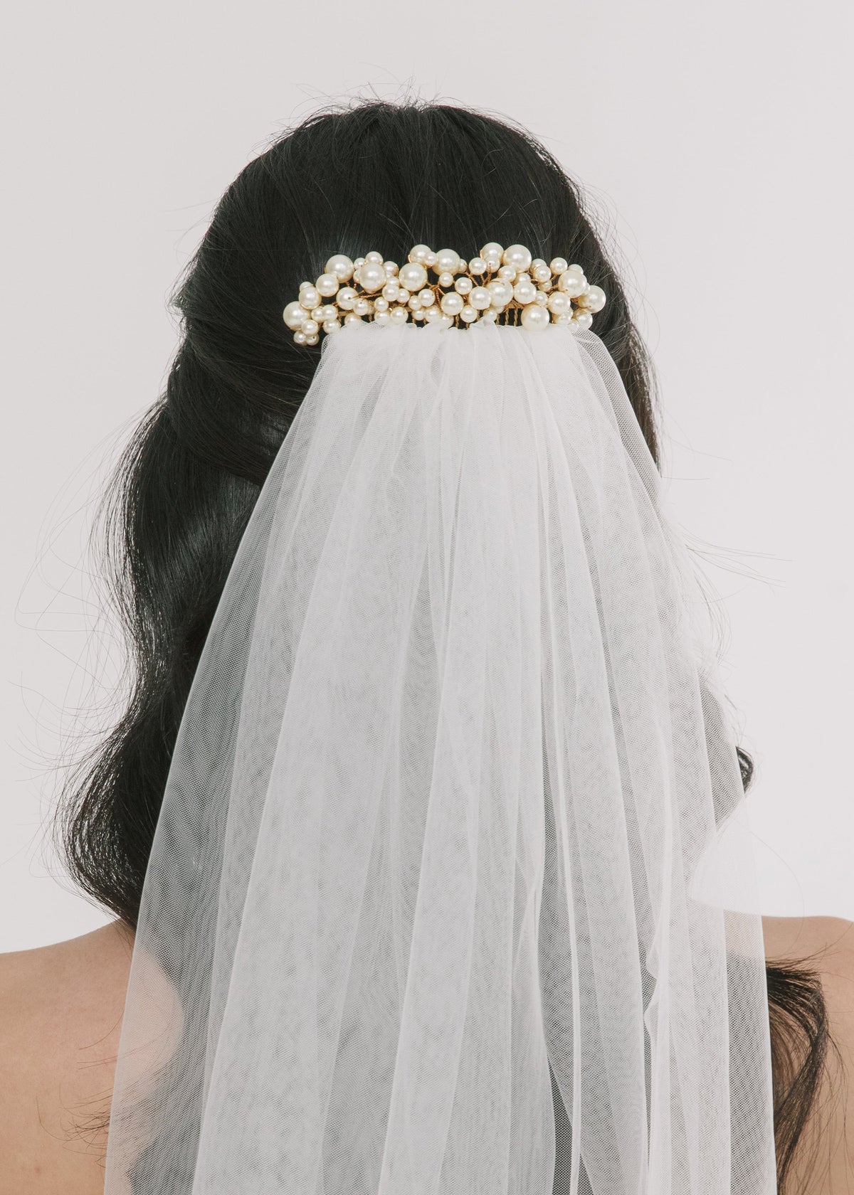 Rear view of Reagan comb in pearl showcasing clustered pearls on gold with attached white tulle veil on light background
