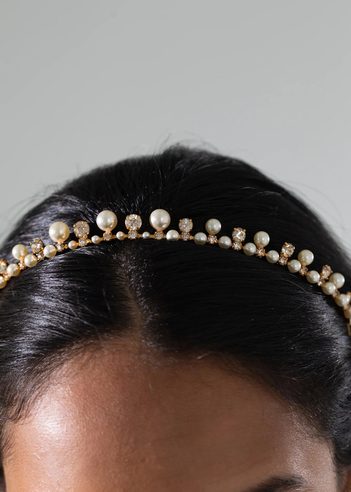 Close up of Corisande Tiara in Pearl Gold on dark hair, showing gold plated band with alternating pearls and crystals