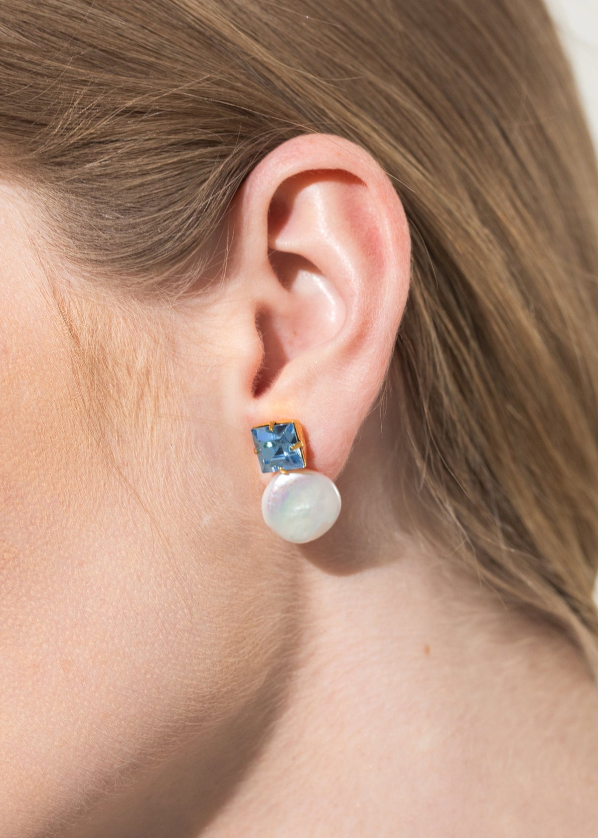 Close-up of Junia Earrings in Sky showcasing a square-cut crystal and freshwater baroque pearl worn on an ear