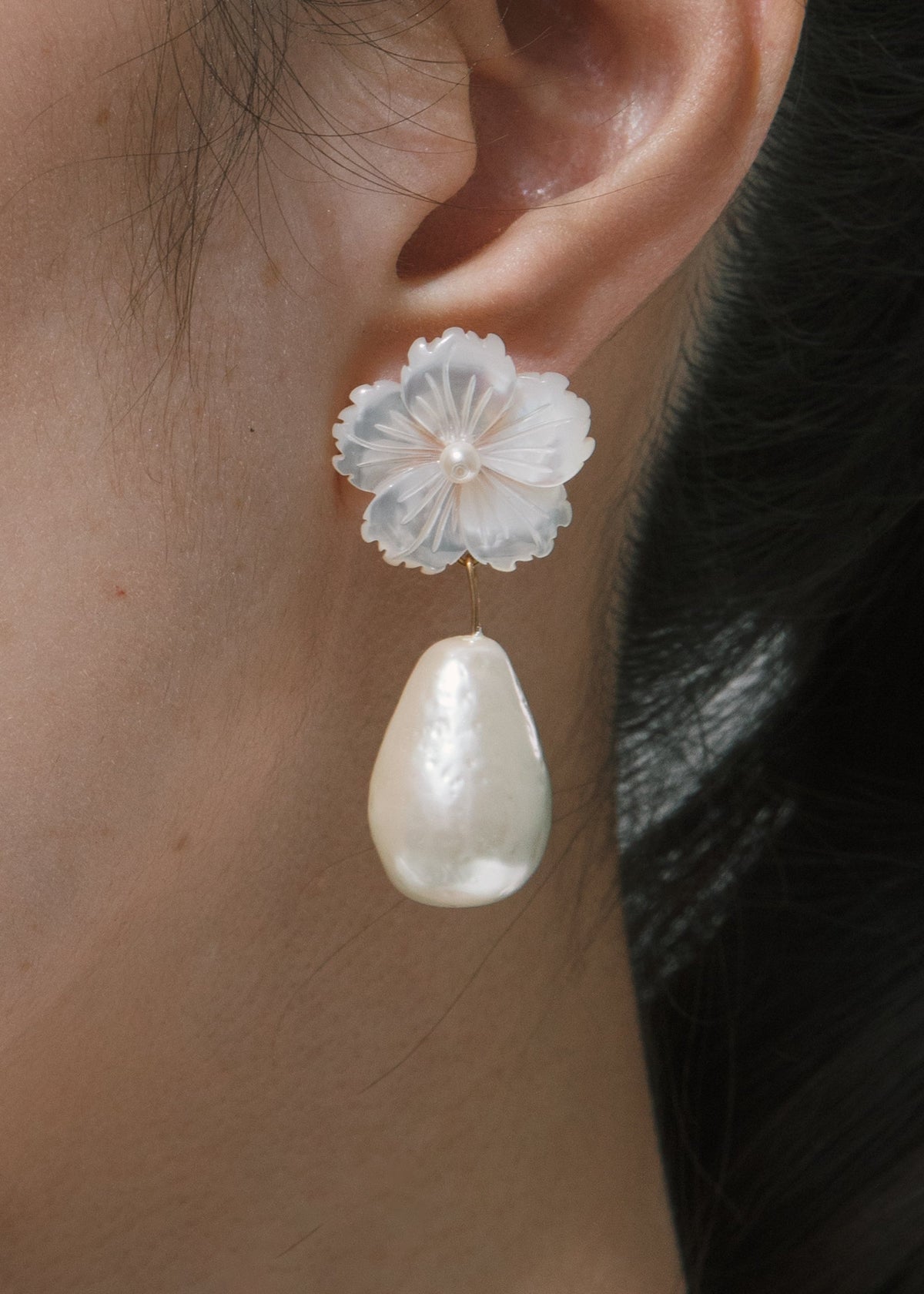 Close-up of Carlla Earrings in Mother Of Pearl showcasing a mother of pearl flower and pearl drop worn on an ear