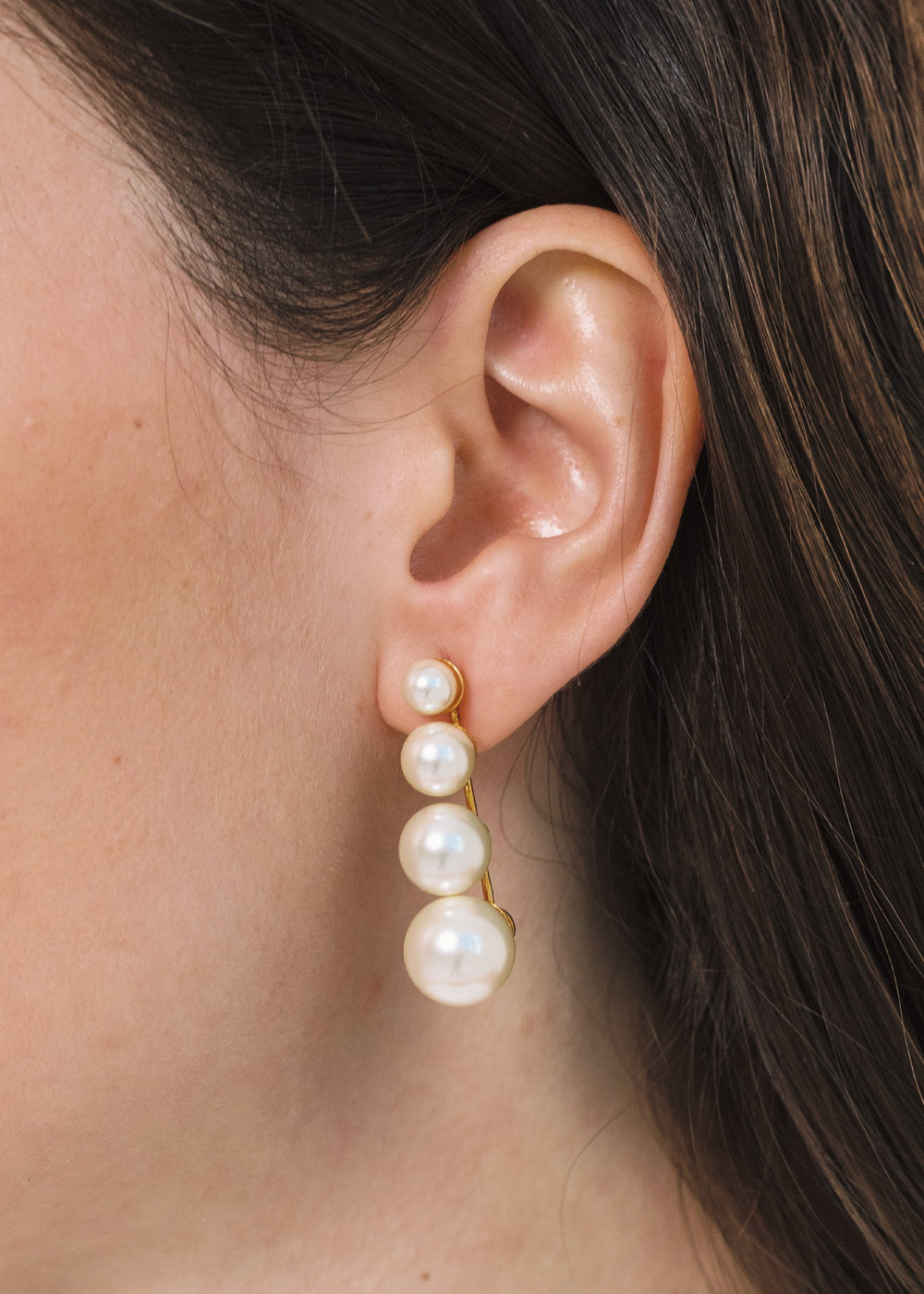 Close-up of Palma Earrings in Pearl showing four graduated pearls on a gold bar worn on model’s ear