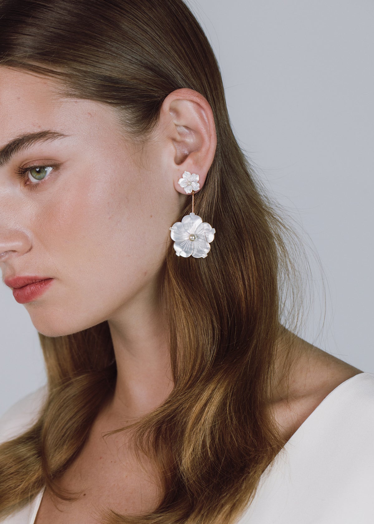 Close-up side view of Zinnia Earrings showcasing carved mother-of-pearl flower drops with pearl centers on a model