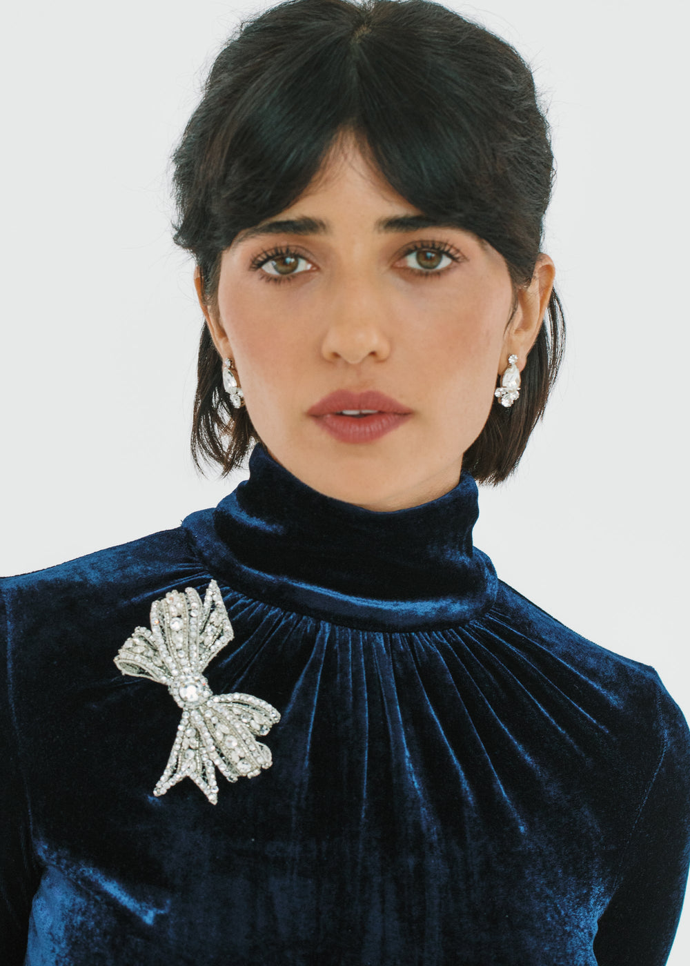 Front view of Gracelyn Brooch in Crystal showcasing crystal-encrusted bow design pinned to a navy velvet high-neck top