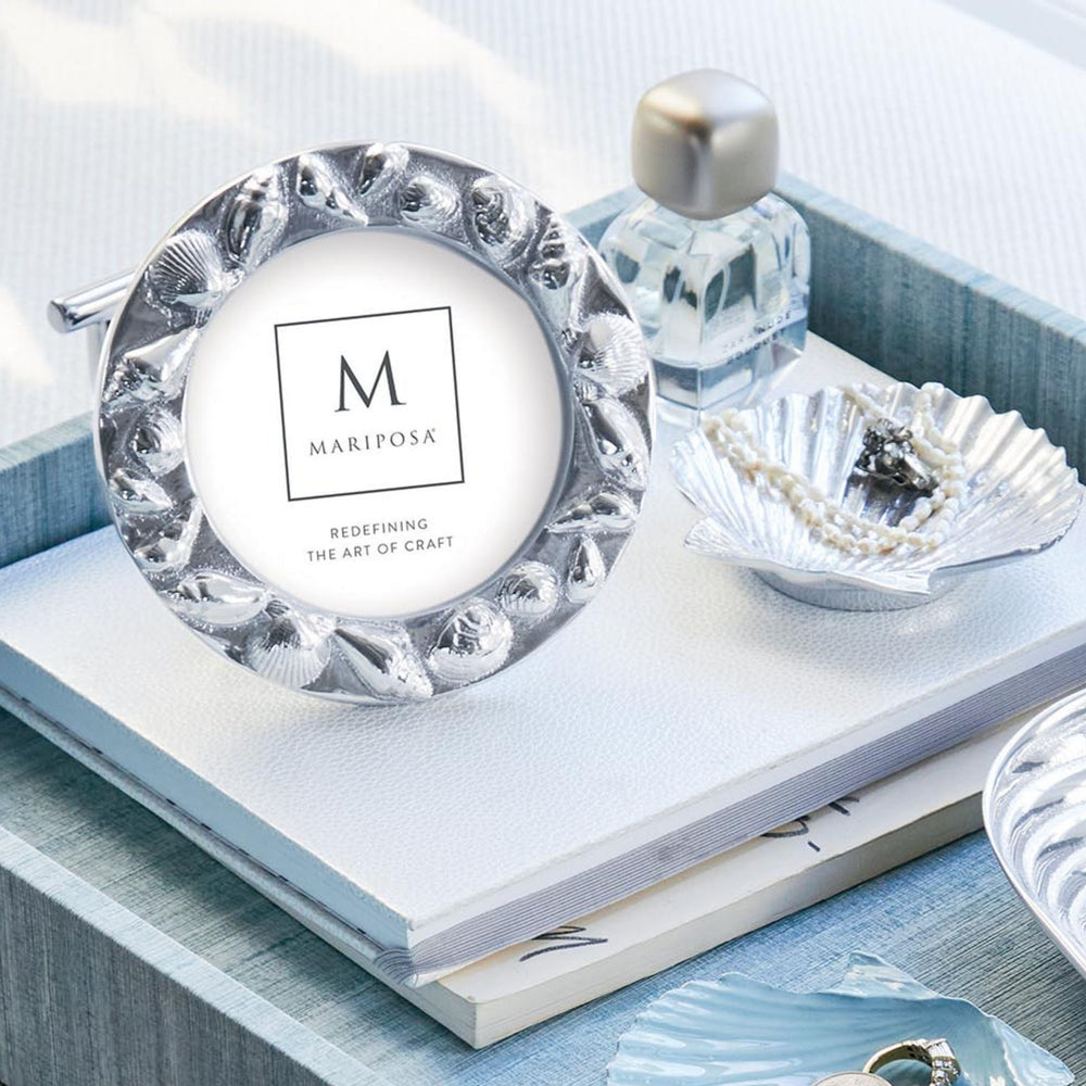 Front view of Mariposa round seashell border 4x4 frame showcasing sculpted seashell border and polished silver finish on a light blue tray