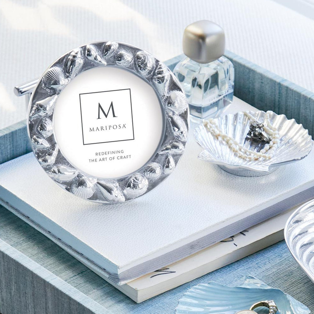 Front view of Mariposa round seashell border 4x4 frame showcasing sculpted seashell border and polished silver finish on a light blue tray