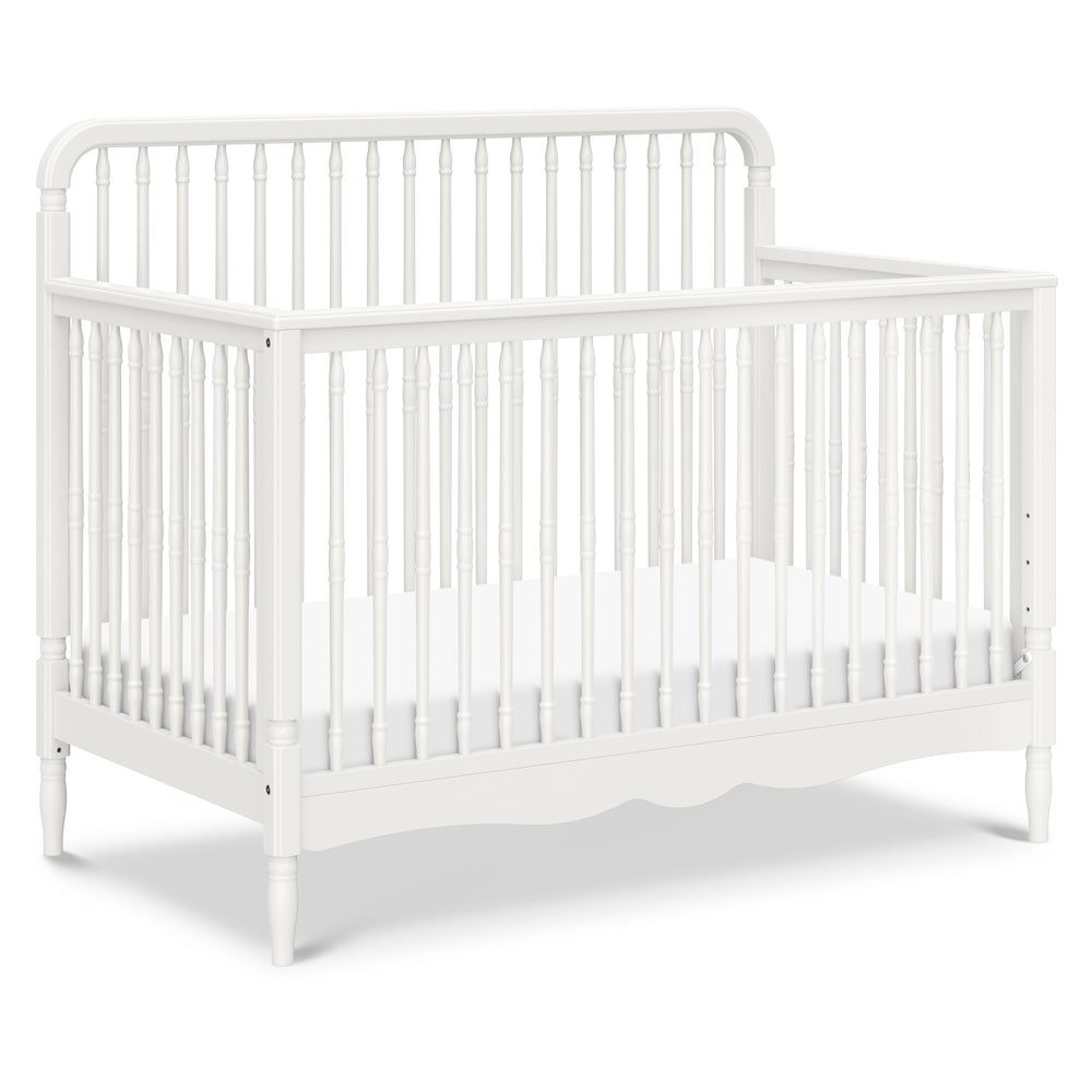 Three-quarter view of Liberty 4-in-1 convertible spindle crib in warm white showcasing thick turned spindles and scalloped base on white background
