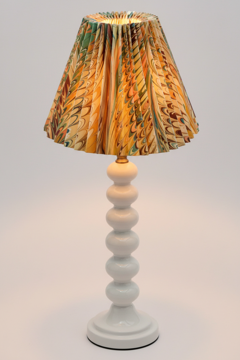 Lit hand-marbled pleated empire lampshade on white stacked base