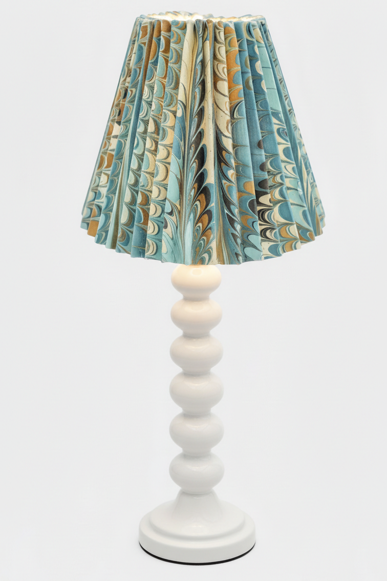 White table lamp with blue and gold marbled pleated empire lampshade, illuminated