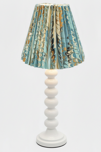White table lamp with blue and gold marbled pleated empire lampshade, illuminated