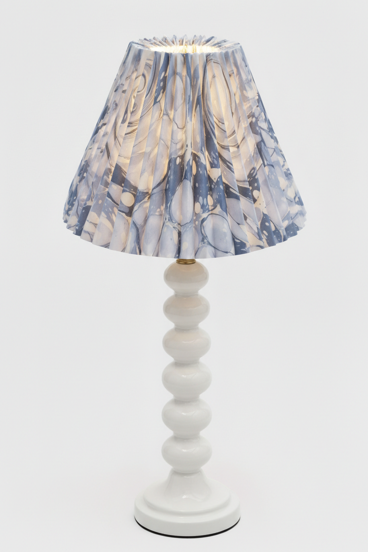 Inner Child table lamp with white stacked base and hand-marbled pleated shade with ocean wave blue patterns lit