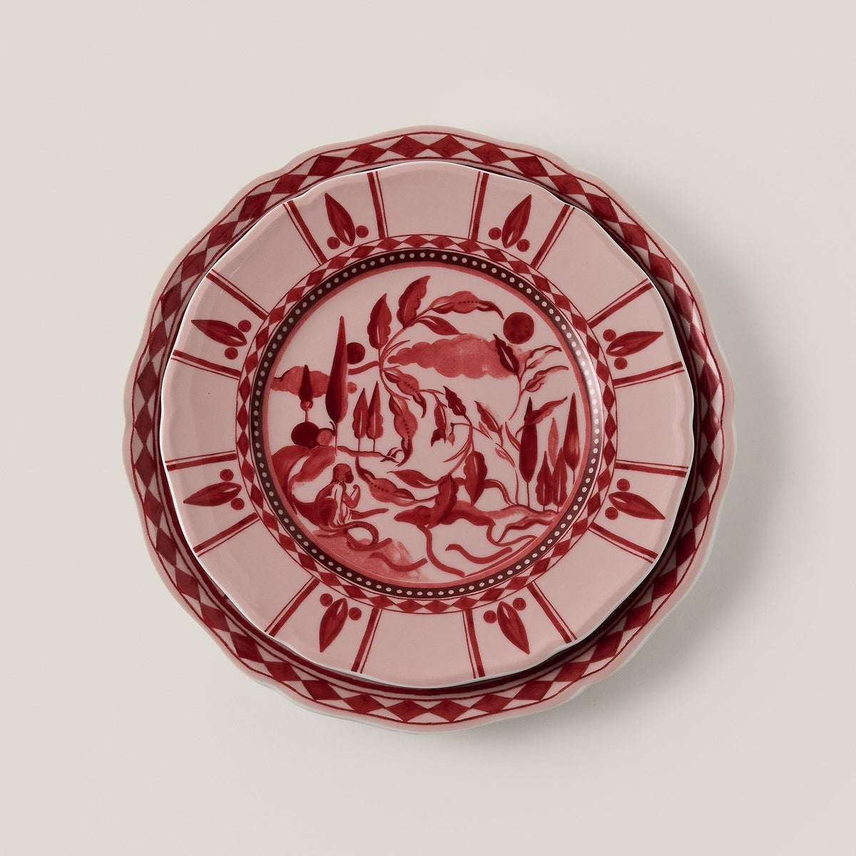 Top-down view of Rêverie des Pins dessert plate in Carmin showcasing red gouache landscape and scalloped patterned rim on beige background