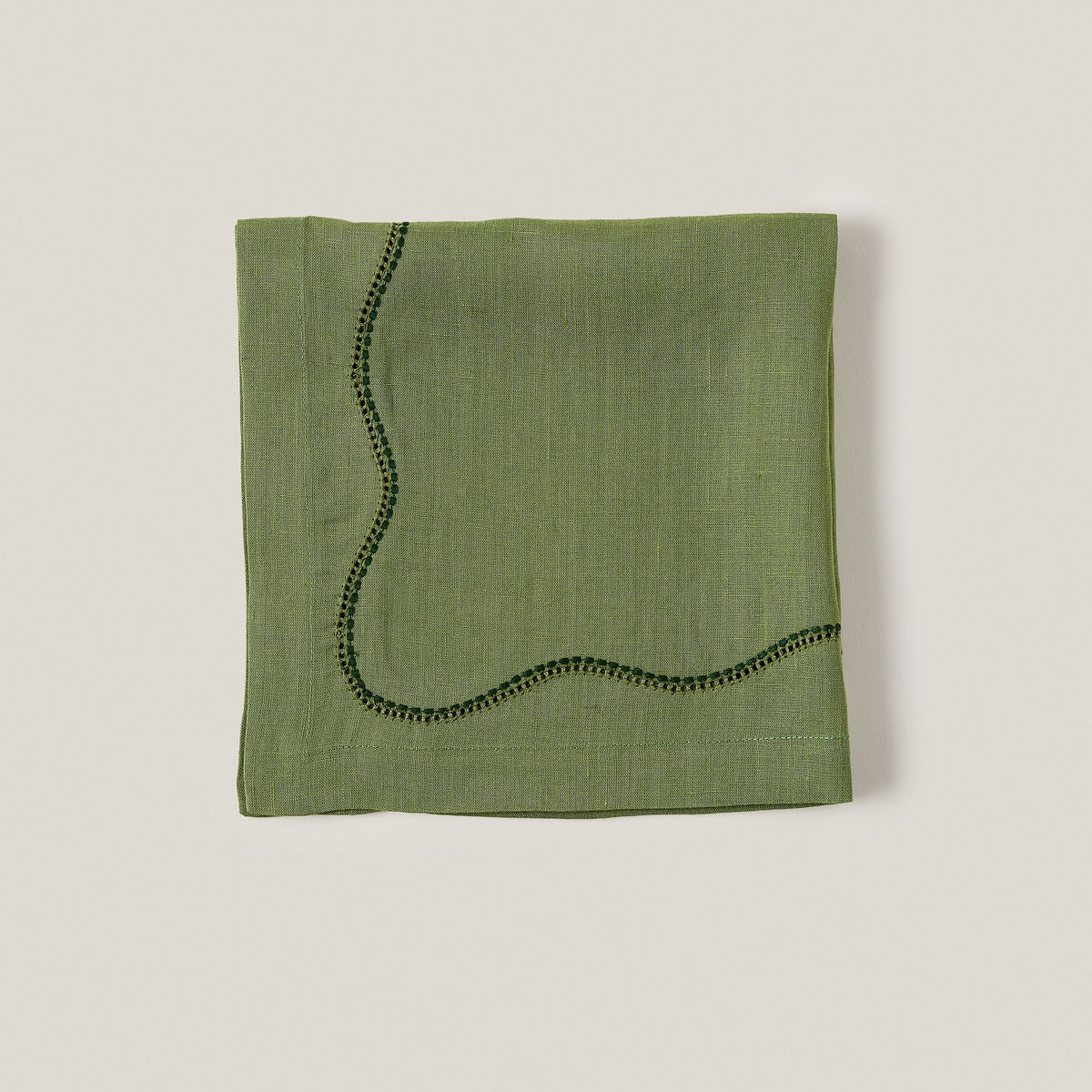Close-up of Le Chemin Napkin in Moss showcasing linen and hand-appliqué detailing on a white background