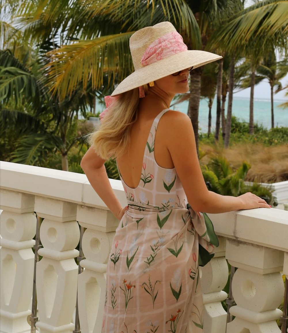 Woman on a balcony wearing Hollyhock sun hat with vintage pink ribbon and rose quartz toggle, tropical palms and ocean background