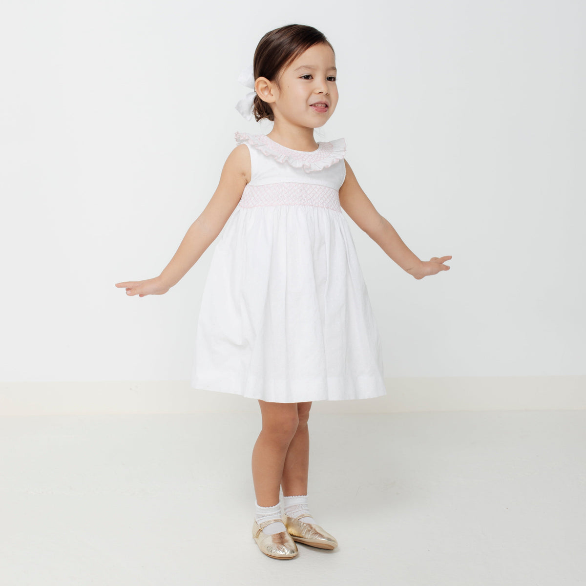 Front view of Tatiana Dress showcasing hand-smocked ruffle collar and pink smocked waistband on a white background