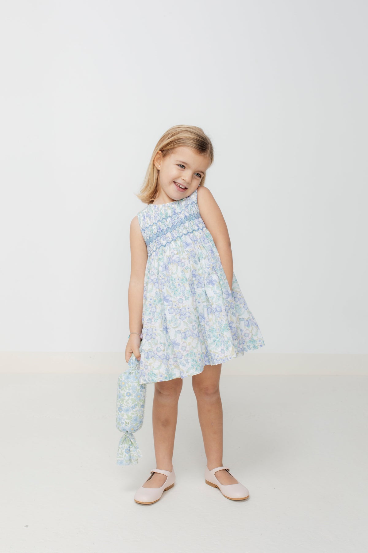 Front of Carlota Dress on child model, blue-green floral smocked bodice, ruffled trims and full skirt on white background