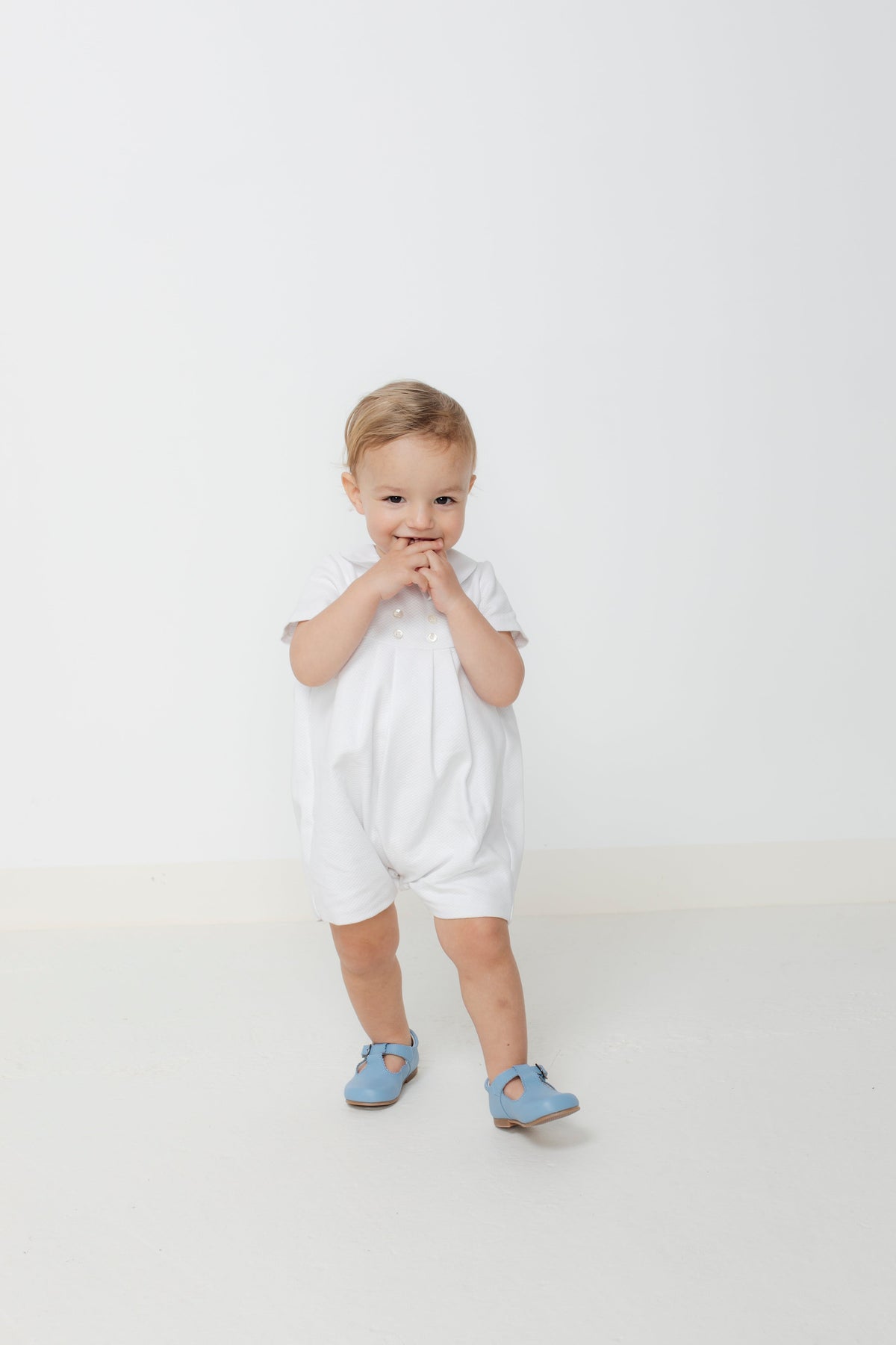 Front view of Felipe Bubble white piqué romper on a toddler showing pleated front and Peter Pan collar against a plain white background