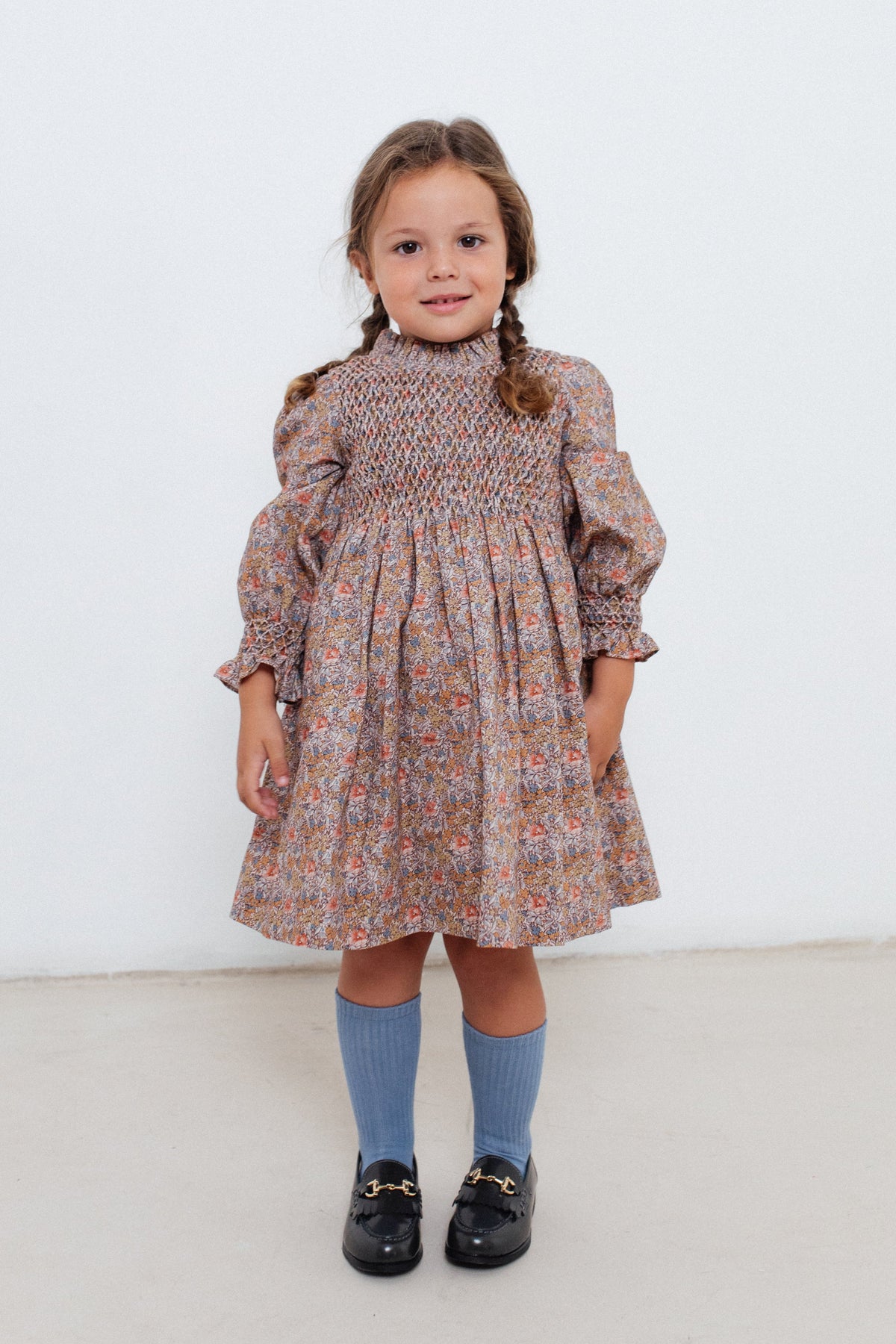 Front view of Simona Dress in Rust Floral on a child, showing hand-smocked bodice, puff sleeves, and gathered skirt