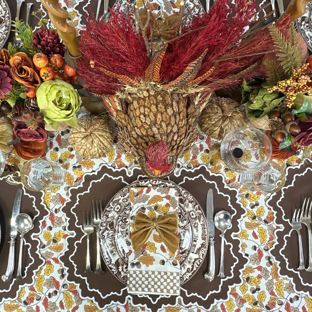 Thanksgiving table setting with turkey centerpiece, fall decorations, and place settings. Acorn leaves hand block printed tablecloth, Whitley placemat and napkin and velvet gold napkin bow ties