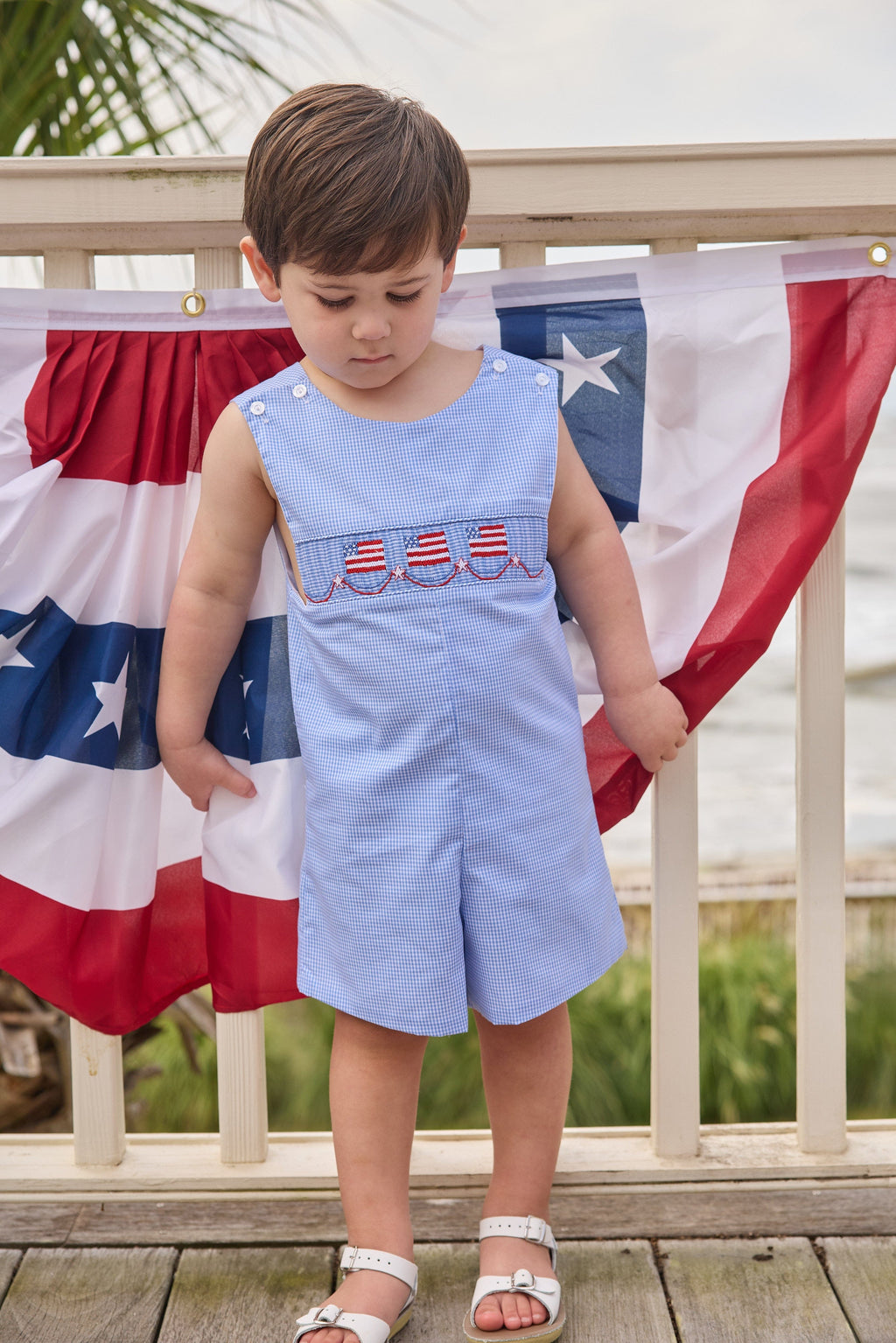 Little English traditional children's clothing.  Classic john john for toddler boys in royal blue mini gingham with American flag smocking at the chest