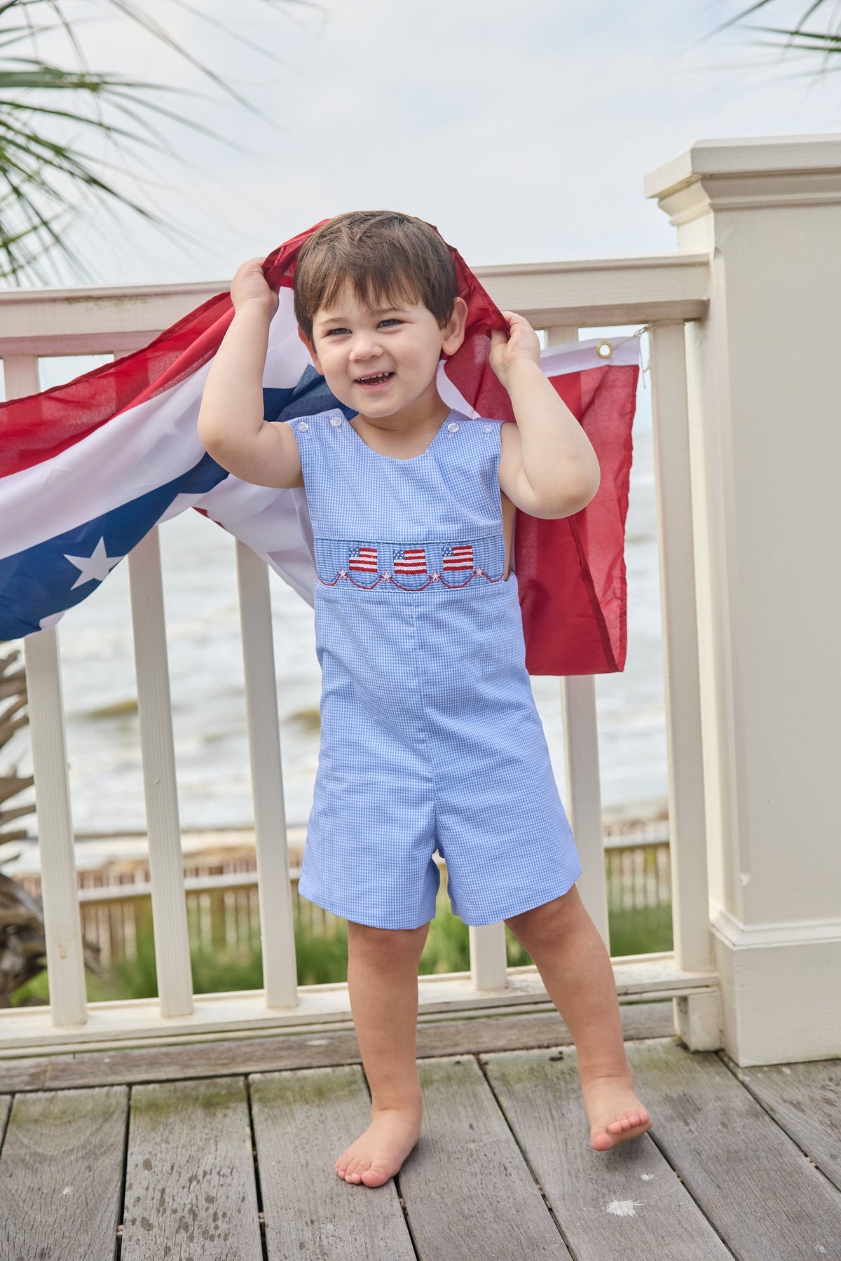 Little English traditional children's clothing.  Classic john john for toddler boys in royal blue mini gingham with American flag smocking at the chest