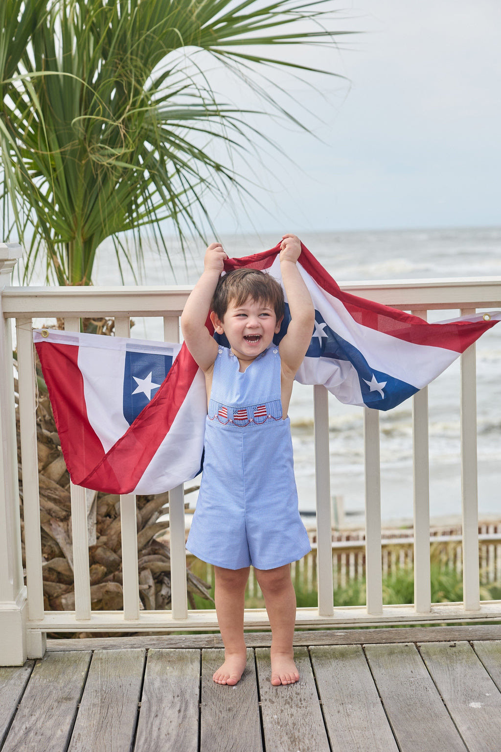 Little English traditional children's clothing.  Classic john john for toddler boys in royal blue mini gingham with American flag smocking at the chest