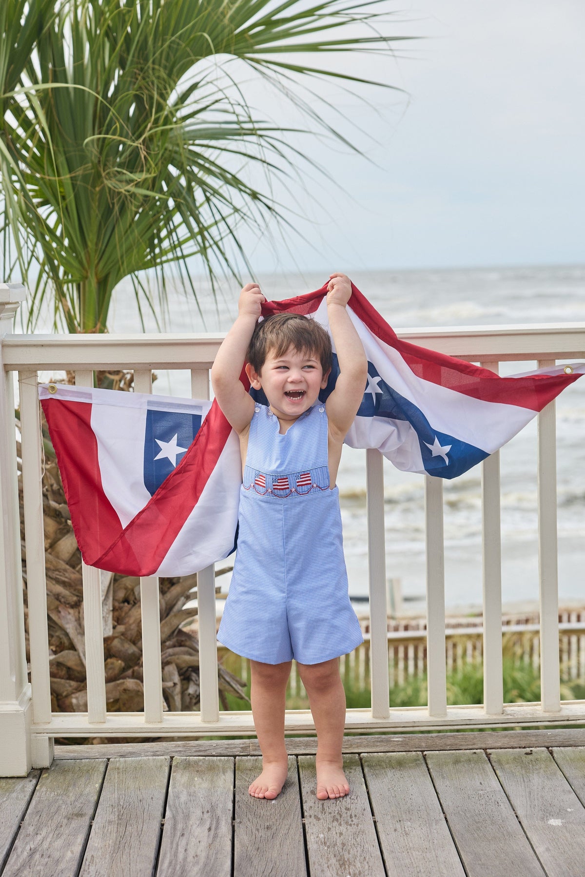 Little English traditional children's clothing.  Classic john john for toddler boys in royal blue mini gingham with American flag smocking at the chest