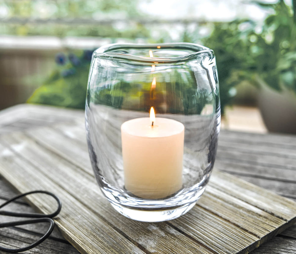 Close-up of Burlington Hurricane glass candle holder showing handblown shape with lit pillar candle on wooden table outdoors