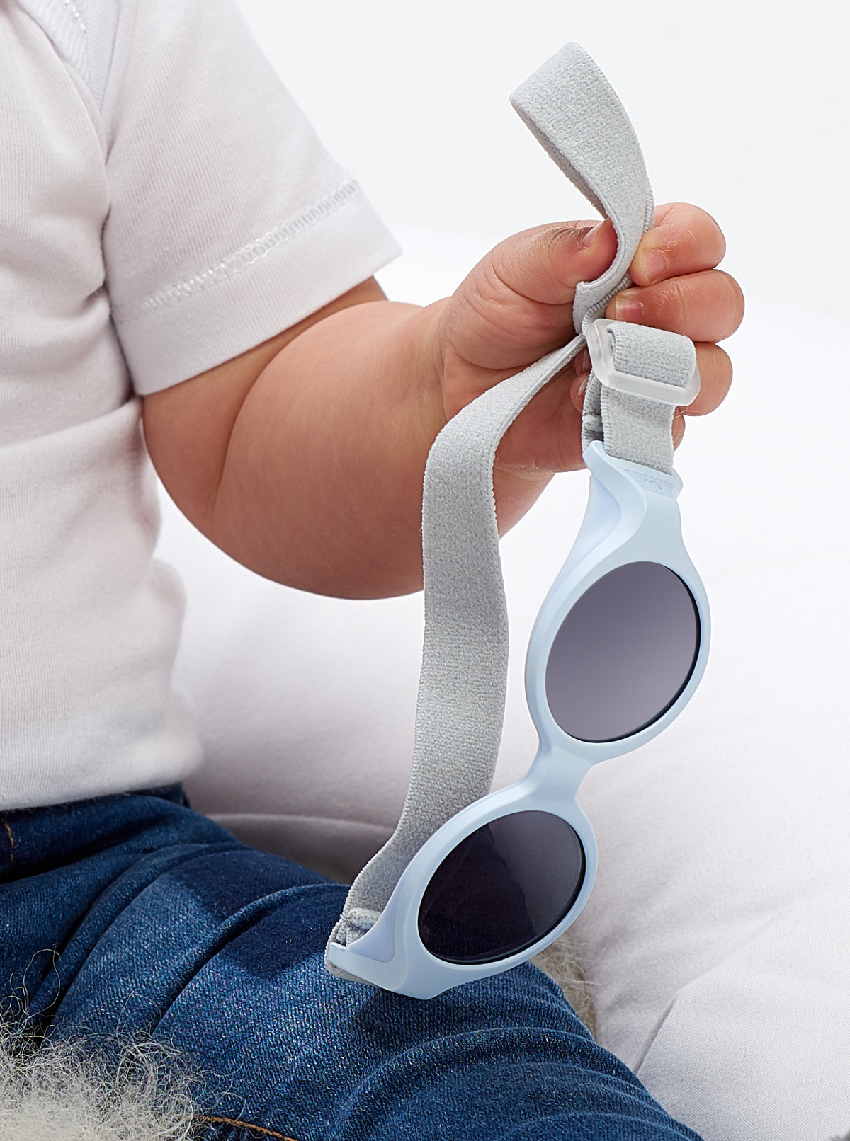 Close-up view of Glee Infant Sunglasses in Pearl Blue showcasing its elasticated headband and held in a hand against a light background