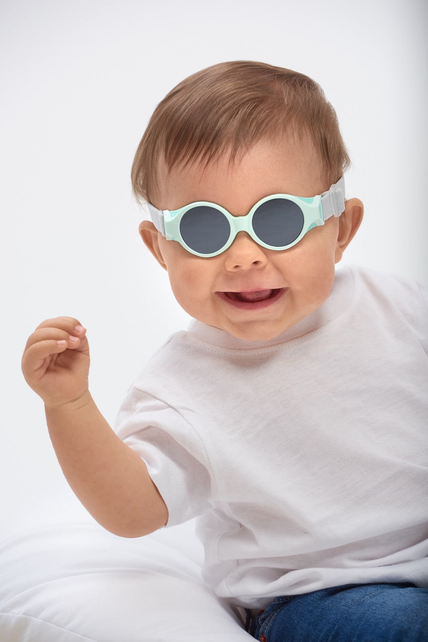 Front view of Glee Infant Sunglasses in Aqua showcasing the elasticated headband on a smiling baby with a light background